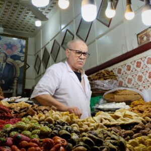 Photo by Taha El Oihaj Man in a pastry shop surrounded by traditional sweets and desserts under warm lighting.